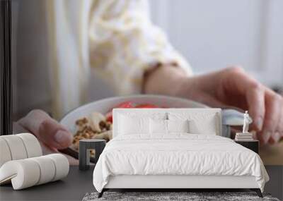 Woman eating tasty granola with banana, cashew and strawberries at wooden table indoors, closeup Wall mural