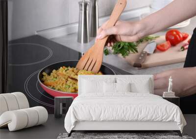 Woman frying rice with meat and vegetables on induction stove in kitchen, closeup Wall mural