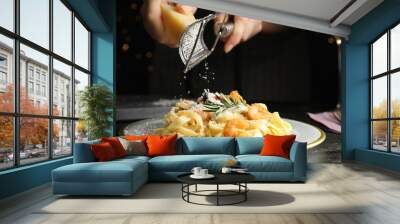 Woman grating cheese onto pasta with shrimps on black table, closeup Wall mural