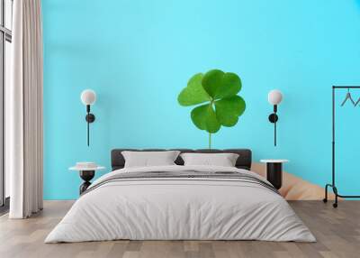 Woman holding beautiful green four leaf clover on light blue background, closeup Wall mural