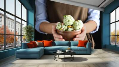 Woman holding bowl full of pistachio ice cream on black background, closeup Wall mural