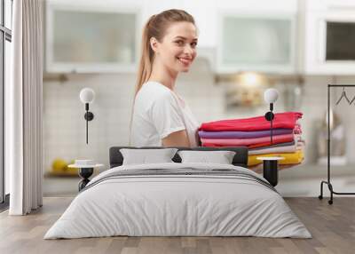 Woman holding folded clean clothes in kitchen. Laundry day Wall mural