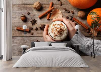 Woman holding glass of tasty pumpkin spice latte on wooden table, flat lay composition Wall mural