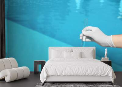 Woman holding glass tube with sample of swimming pool water to check PH level outdoors, closeup. Space for text Wall mural