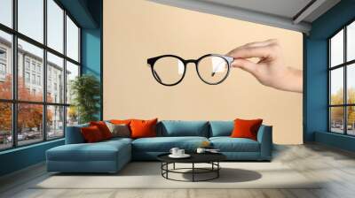 Woman holding glasses on beige background, closeup. Ophthalmologist prescription Wall mural