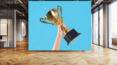 Woman holding gold trophy cup on light blue background, closeup Wall mural