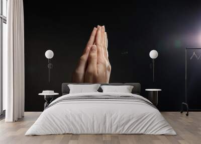 Woman holding hands clasped while praying against light in darkness, closeup. Space for text Wall mural