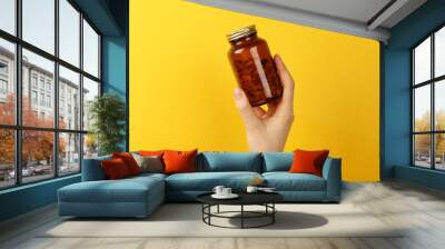 Woman holding jar with vitamin capsules on yellow background, closeup Wall mural