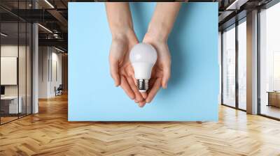 Woman holding light bulb on color background, top view Wall mural