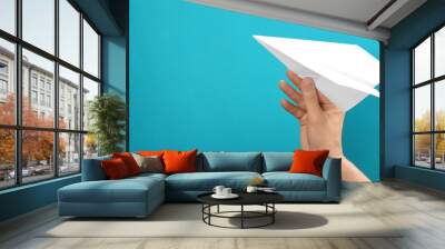 Woman holding paper plane on light blue background, closeup. Space for text Wall mural