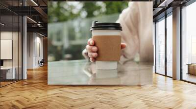 Woman holding paper takeaway cup at glass table outdoors, closeup. Coffee to go Wall mural