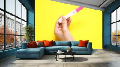 Woman holding pregnancy test on yellow background, closeup Wall mural