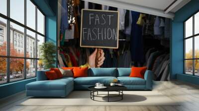 Woman holding small chalkboard with phrase FAST FASHION in clothes store, closeup. Space for text Wall mural