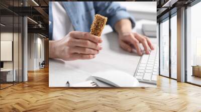 Woman holding tasty granola bar working with computer at light table in office, closeup Wall mural