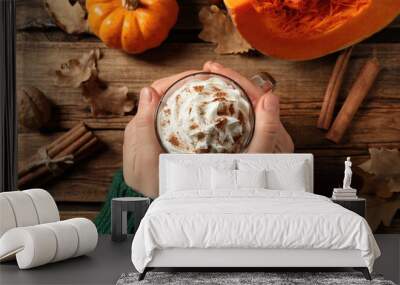 Woman holding tasty pumpkin latte at wooden table, top view Wall mural