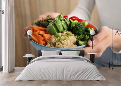 Woman holding vegan bowl with avocados, carrots and broccoli indoors, closeup Wall mural