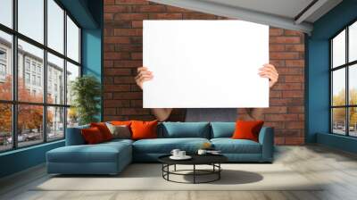 Woman holding white blank poster near red brick wall. Mockup for design Wall mural