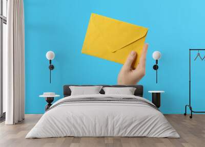 Woman holding yellow paper envelope on light blue background, closeup Wall mural