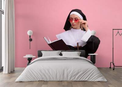 Woman in nun habit and sunglasses reading Bible against pink background Wall mural