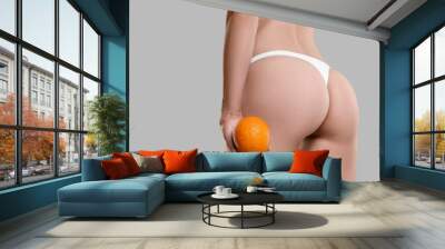 Woman in underwear with orange on light grey background, closeup. Cellulite problem Wall mural