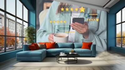 Woman leaving service feedback with smartphone while drinking coffee, closeup. Reviews and stars near device Wall mural