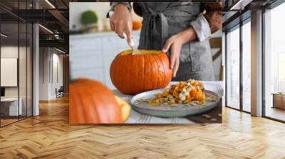 Woman making pumpkin jack o'lantern at table indoors. Halloween celebration Wall mural