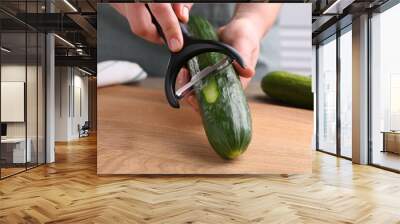 Woman peeling cucumber at wooden table indoors, closeup Wall mural