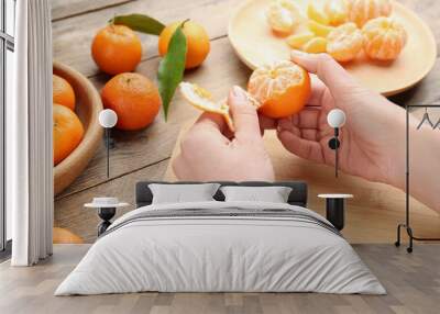 Woman peeling fresh ripe tangerine at wooden table, closeup Wall mural