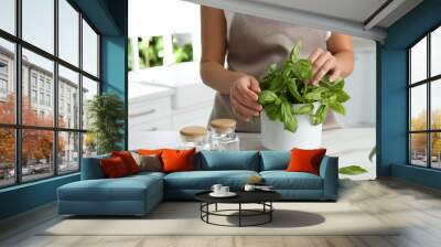 Woman picking fresh basil at white table in kitchen, closeup Wall mural