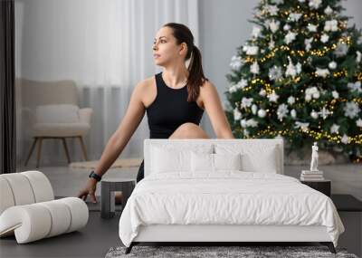 Woman practicing yoga against Christmas tree indoors Wall mural