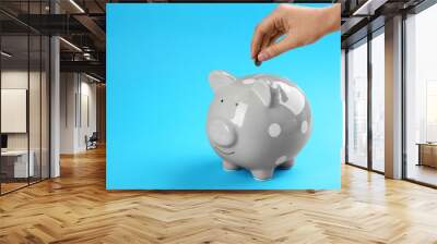 Woman putting coin into piggy bank on blue background, closeup Wall mural