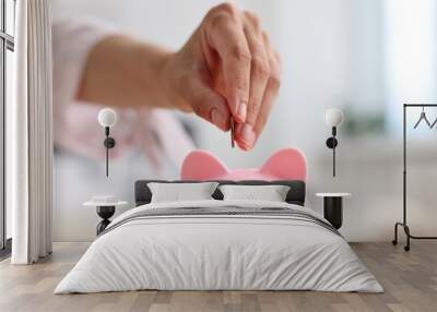 Woman putting coin into pink piggy bank at home, closeup Wall mural