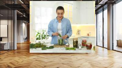 Woman putting cucumber into pickling jar at table in kitchen Wall mural