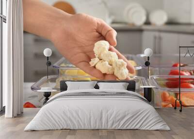 Woman putting cut cauliflower into box and containers with raw vegetables in kitchen, closeup Wall mural