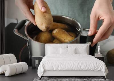 Woman putting potato into metal pot on stove, closeup Wall mural