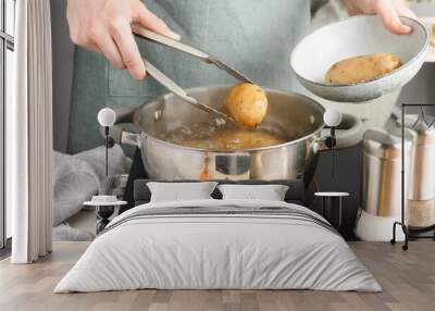 Woman putting raw potato into pot on stove, closeup Wall mural