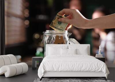 Woman putting tips into glass jar on wooden table indoors, closeup Wall mural