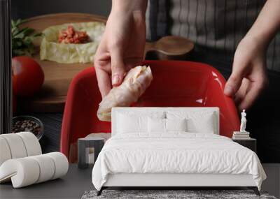 Woman putting uncooked stuffed cabbage roll into baking dish at black table, closeup Wall mural