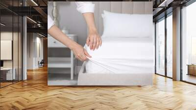 Woman putting white fitted sheet over mattress on bed indoors, closeup Wall mural