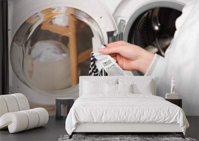 Woman reading clothing label with care symbols and material content on striped shirt near washing machine, closeup Wall mural