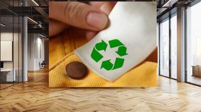 Woman showing clothing label with recycling symbol on yellow jeans, closeup Wall mural