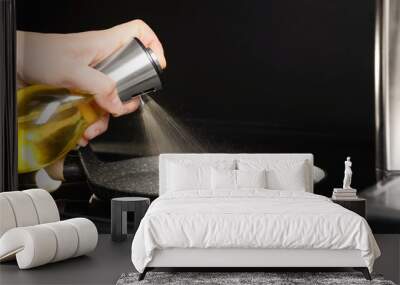 Woman spraying cooking oil onto frying pan on stove, closeup Wall mural