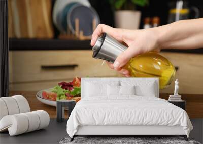 Woman spraying cooking oil onto salad on wooden table in kitchen, closeup Wall mural