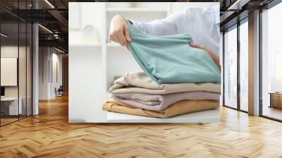 Woman stacking clean clothes at white table indoors, closeup Wall mural