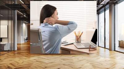 Woman suffering from neck pain at table in office Wall mural