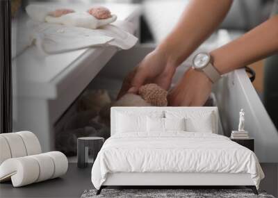 Woman taking baby clothes from chest of drawers, closeup Wall mural