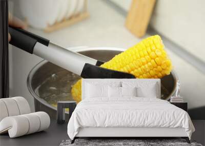 Woman taking boiled corn from pot with tongs in kitchen, closeup Wall mural