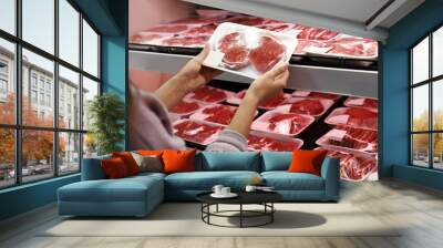 Woman taking packed pork meat from shelf in supermarket Wall mural