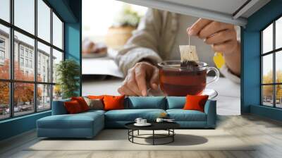 Woman taking tea bag out of cup at white wooden table indoors, closeup. Space for text Wall mural