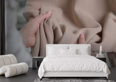 Woman touching clothes made of soft beige fabric indoors, closeup Wall mural